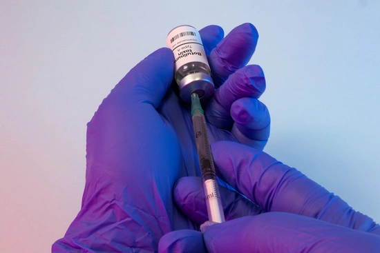 Three clear glass vials with pink caps, clearly labeled "Botulinum Toxin Type A for Injection, 100 units/vial," are positioned in front of several white, insulated gel cold packs.