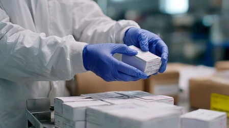 A laboratory technician in protective gear carefully preparing a temperature-sensitive peptide shipment using standardized protocols.